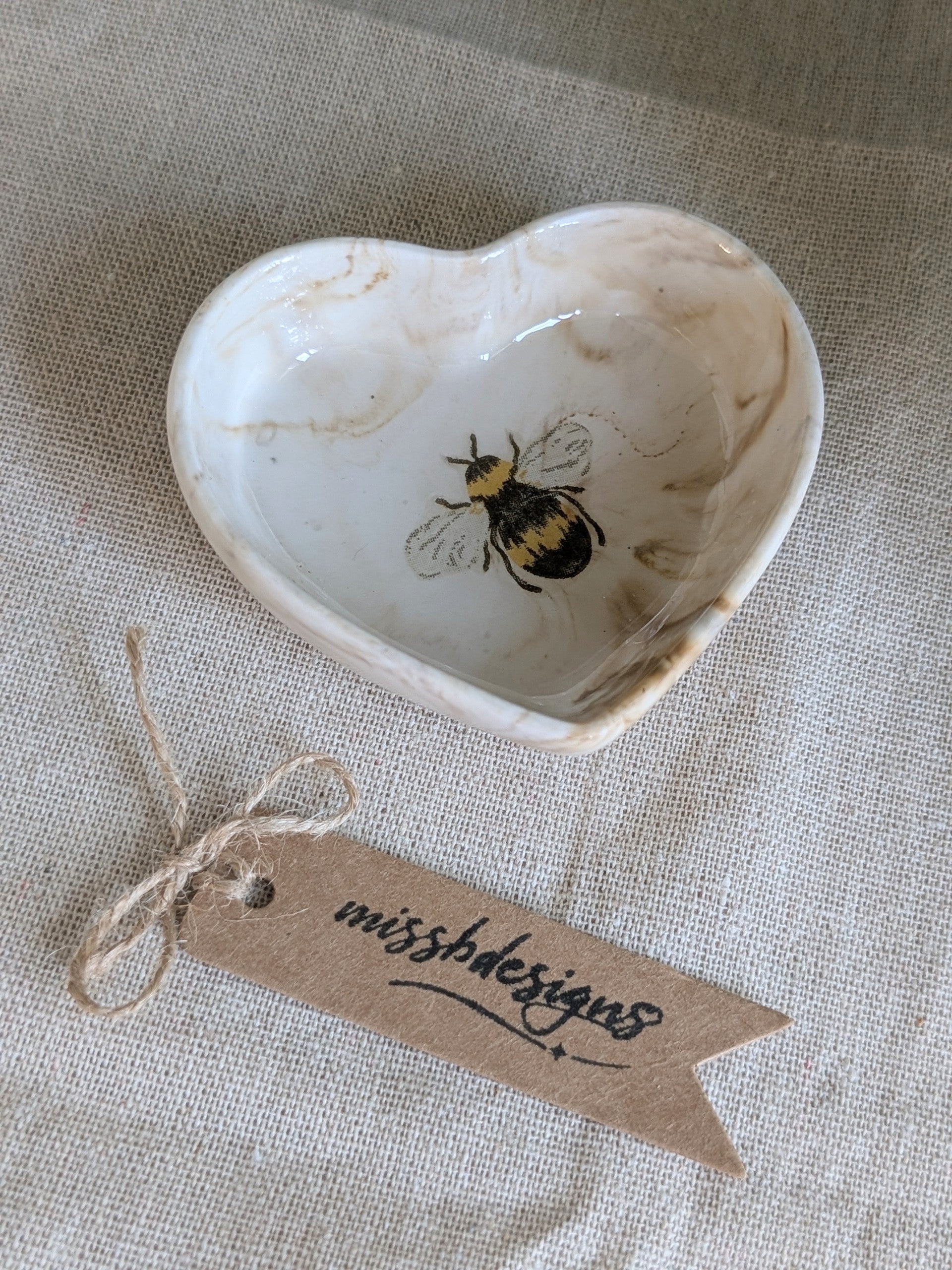 A small heart-shaped natural beige ceramic ring trinket dish with a printed bumble bee design inside perfect gift
