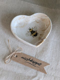 A small heart-shaped natural beige ceramic ring trinket dish with a printed bumble bee design inside perfect gift